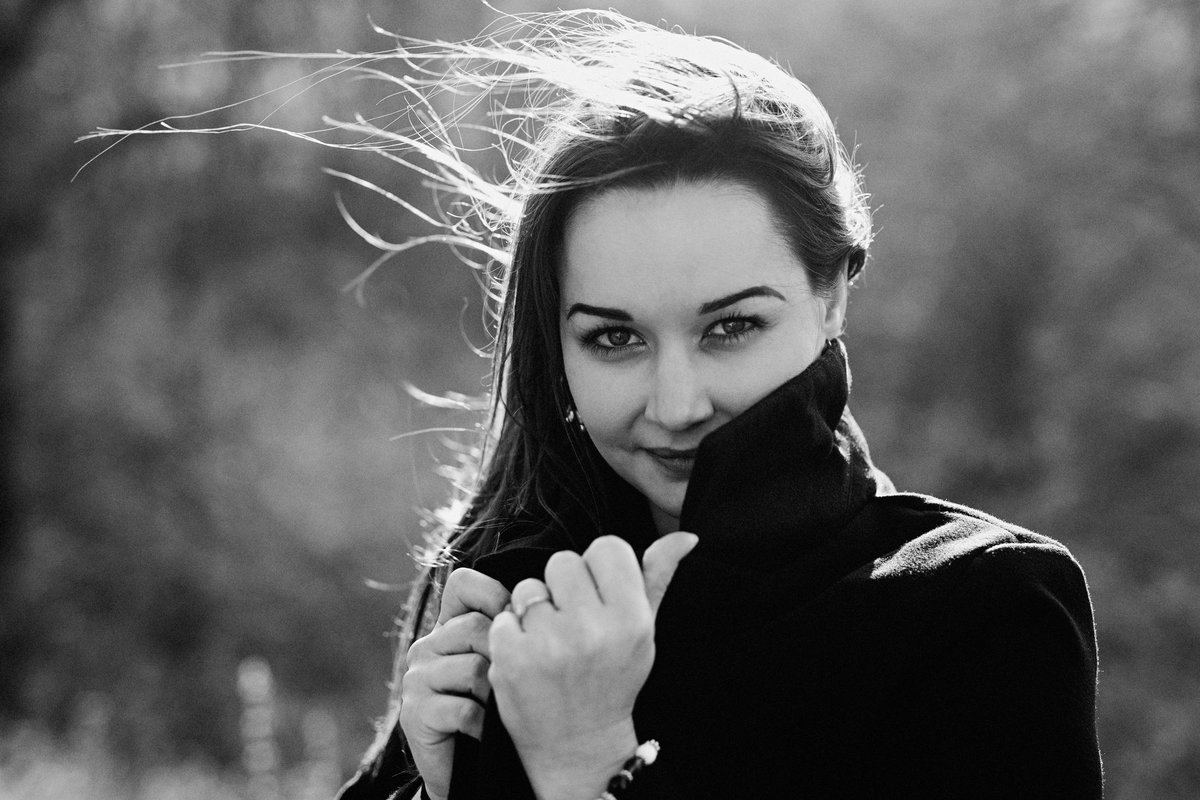 A black and white portrait of a woman outdoors, her hair caught by the wind